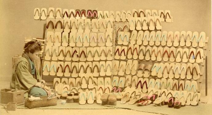 Farvelagt fotografi, der forestiller en japansk kvinde der laver traditionelt håndværk - sko. Billedet er taget i studie og de traditionelle håndværk var på vej til at forsvinde, men man ville gerne fremstille dem i de billeder folk så af Japan.