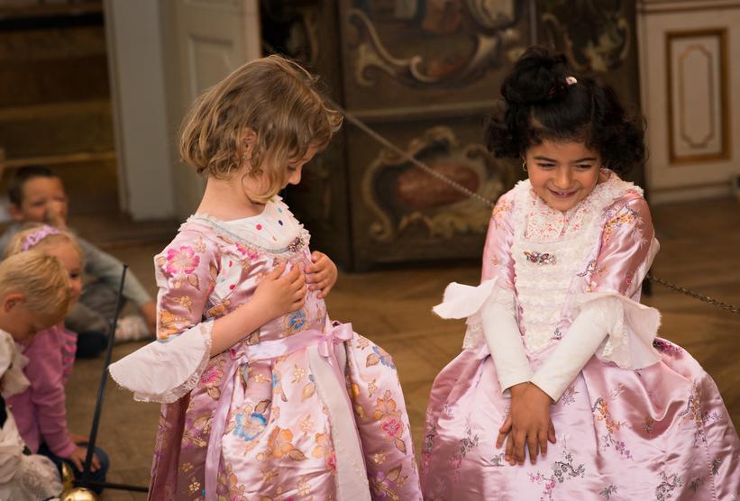 To piger prøver at være ægte adels-damer i flotte, lyserøde, silkekjoler.